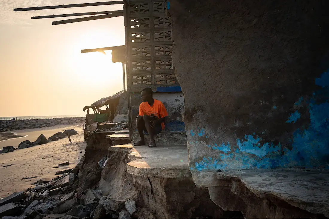 A man sits in front of a crumbling house in Accra, Ghana